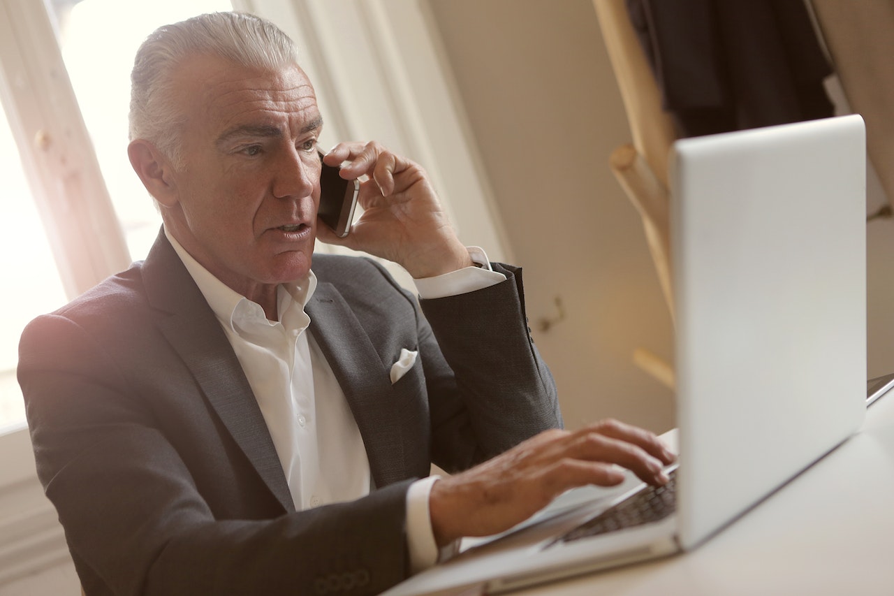 older man talking on phone and using computer