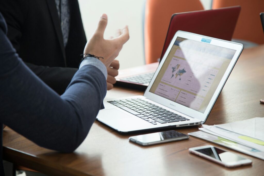 two people are talking with an open laptop on the table showing marketing metrics
