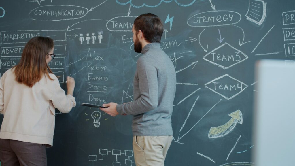 a man and woman are standing in front of a chalkboard talking and creating a marketing strategy