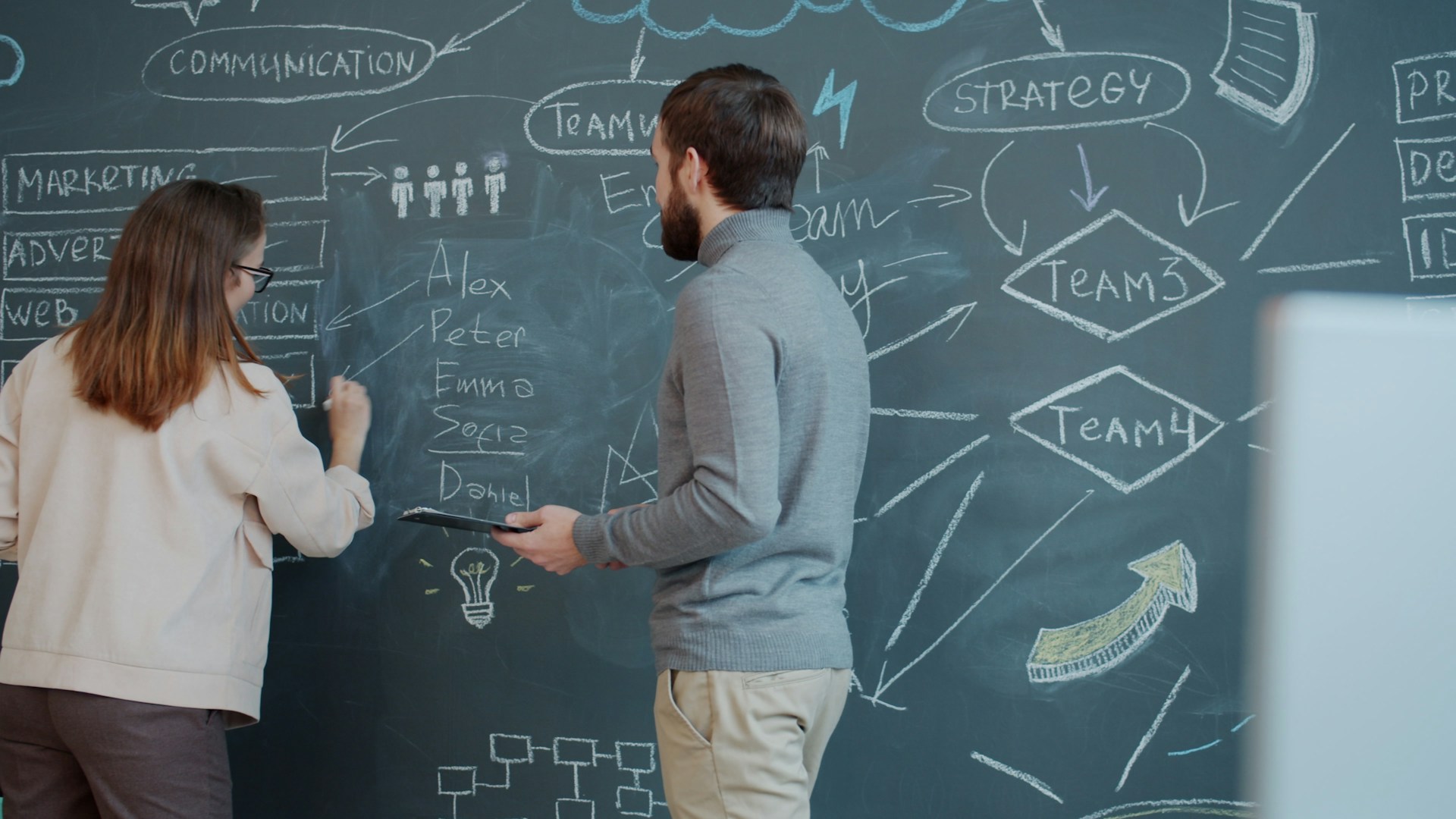 a man and woman are standing in front of a chalkboard talking and creating a marketing strategy